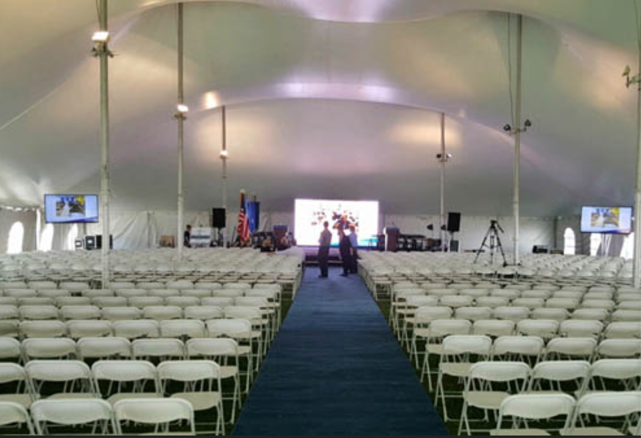 Large outdoor tent event setup with rows of white chairs stage and projection screens by CitiView AV
